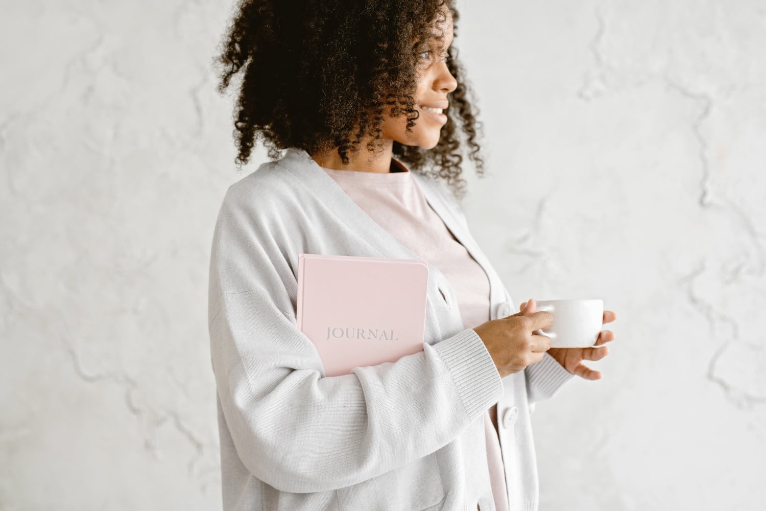 A smiling woman holding an affirmation journal and a white cup
