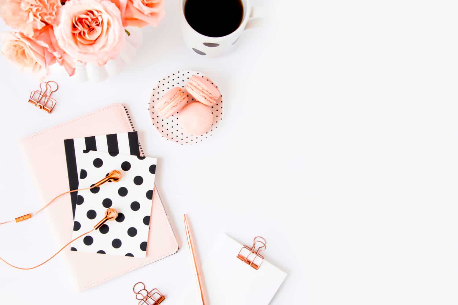 Feminine stationery with rose gold headphones, notebooks, pink macarons and a cup of coffee