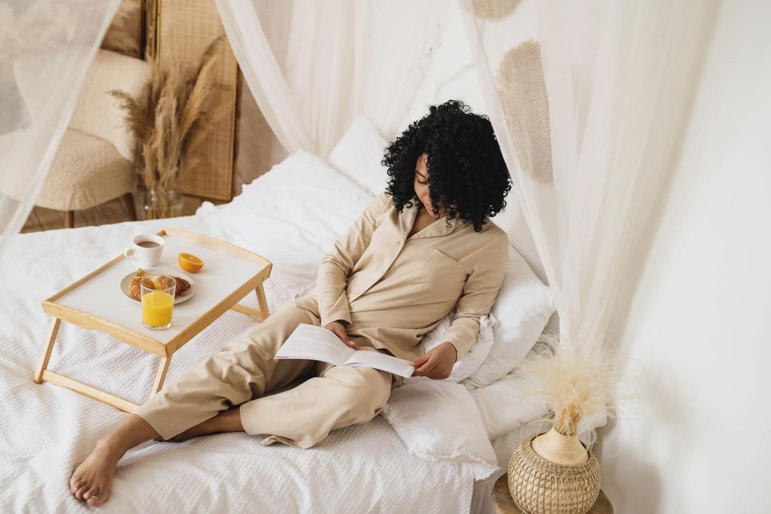 A woman lying on bed, reading a book with a breakfast tray next to her